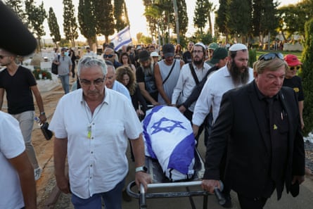 People carry a body wrapped in an Israeli flag on a stretcher through a crowd