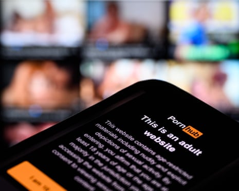 A smartphone screen displays a Pornhub age-restriction warning in a close-up with a blurred background