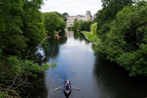 A drone shot of a couple in a rowing boat on a river with a castle in the distance