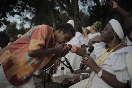 A seated woman holding a microphone accepts a kiss on the hand from a hand.