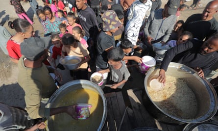 Children dipping food bowls into large containers of what may be grain and soup, seen from above