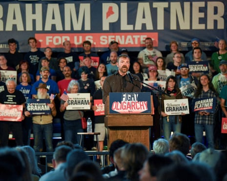 man speaks at lectern marked 'fight oligarchy' as crowd holds signs saying 'women for graham', 'graham platner' and 'veterans for graham'
