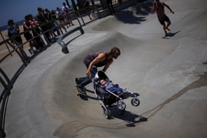 A skateboarder holds a baby doll in a stroller on a slope at a skatepark