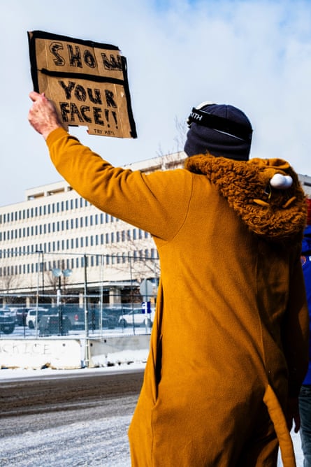 A protester holds a sign that says ‘show your face’