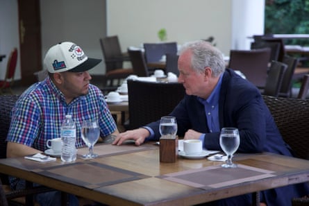 two men speak while seated at a table