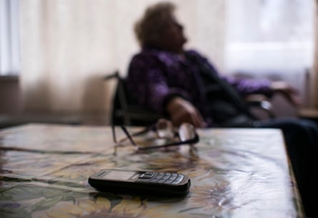 A mobile phone sits on a table near an elderly woman