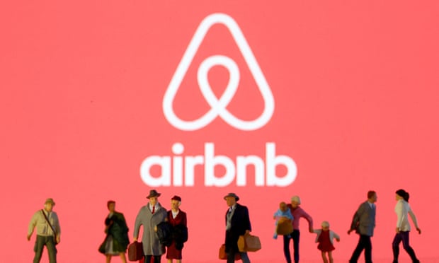 Small toy figures are seen in front of displayed Airbnb logo
