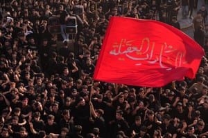 A large red flag with Arabic script is raised above hundreds of people