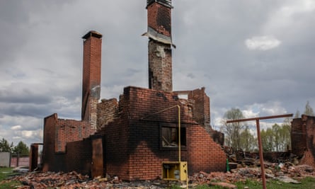 A badly damaged brick house, scorched, with the roof and much of the upper walls missing, but two tall chimney stacks still standing
