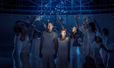 Paris Fitzpatrick and Cordelia Braithwaite as Romeo and Juliet, little by torchlight, being showered by confetti by a group of people around them, everyone dressed in white vests, in an asylum setting