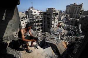 A man sits in a damaged building looking out at other damaged buildings