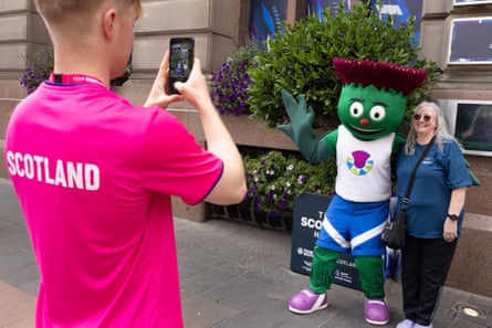 A Team Scotland volunteer in a pink t-shirt with ‘Scotland’ on the back of it takes a photo of a fan with Clyde, an anthropomorphic thistle who is Scotland’s mascot for this year’s Commonwealth Games in Glasgow.