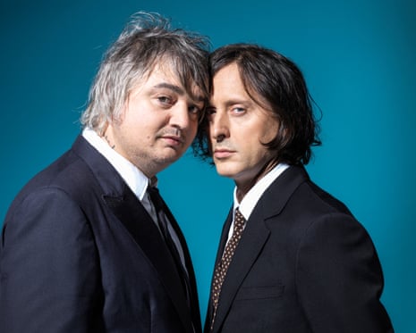 The Libertines’ Pete Doherty (on left) and Carl Barât, standing with heads together against a dark turquoise background
