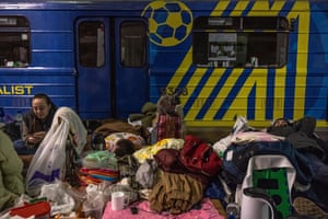 A cat sits on luggage as people stay inside a subway station used as a bomb shelter.