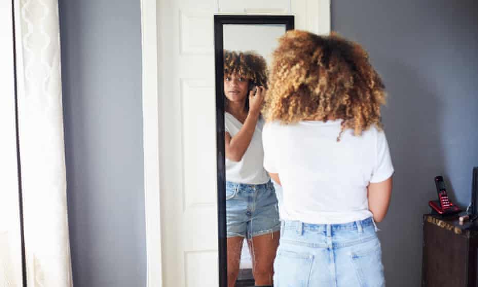 Black woman examining hair in mirror