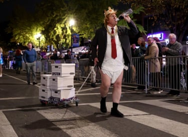 A person dressed as Donald Trump in a nappy towing a cart with boxes marked ‘Epstein’