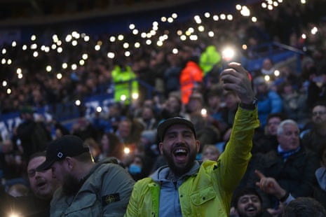 Fans shine lights on their phones as the floodlights fail inside the stadium.