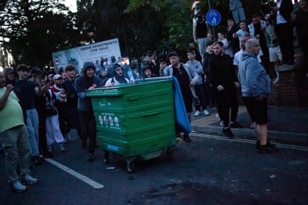 Moffitt, with a blue lanyard, can be seen filming protesters pushing a large bin