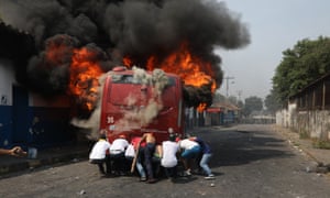 Demonstrators push a bus that was torched during clashes with the Bolivarian national guard in Ureña, Venezuela, on 23 February.