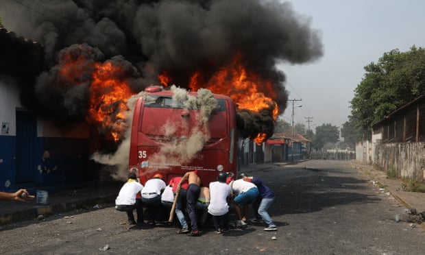 Demonstrators push a bus that was torched during clashes with the Bolivarian national guard in Ureña, Venezuela, on 23 February.