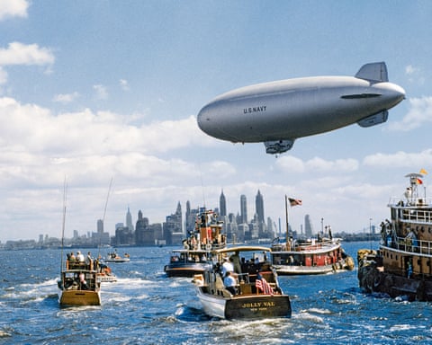 A US Navy airship flies above boats in New York Harbour near the skyline