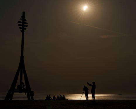 People observe a partial solar eclipse on Crosby beach near Liverpool as the moon covers part of the sun in Liverpool, England.