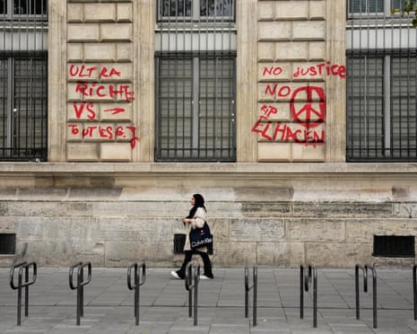 A woman walks past a Paris building wall covered in red protest graffiti
