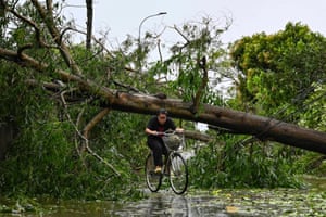 A woman ducks as she cycles under a fallen tree blocking a road