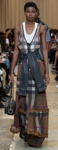 A Black model in a long Burberry dress with a jeans jacket tied around her dress walks towards the camera