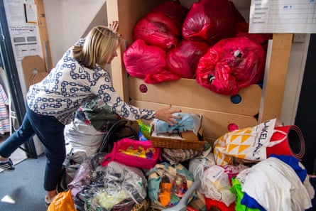 A blond woman in a patterned top and blue jeans putting plastic bags stuffed with items into a cupboard
