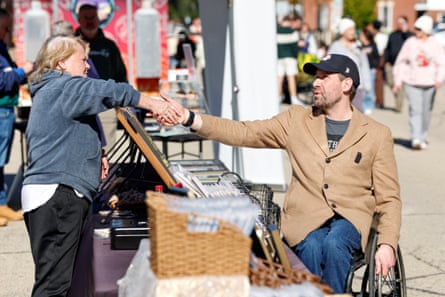 A man in a wheelchair shakes hands with a woman at a market stall.