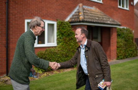 Rout leans in to shake hands with Ramsbottom outside a redbrick house