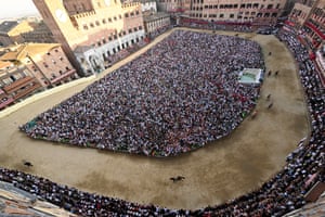 Aerial shot of jockeys racing on a D-shaped track, with crowds both sides of the track