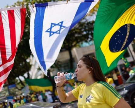 A Bolsonaro supporter drinks from a water bottle beneath Brazilian, Israeli and US flags.