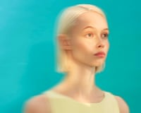 Treated photograph of blond-haired young woman looking vaguely into the distance against a turquoise background with a shadow on her left eye area