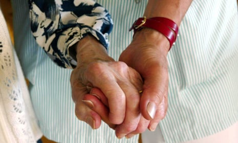 A care assistant holds an elderly lady's hand