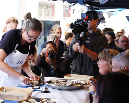 A competitor shucks an oyster in front of a crowd and camera