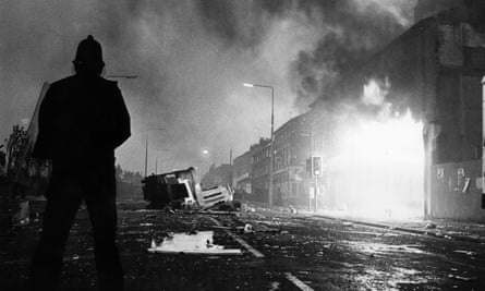 A police officer in riot gear stands among the broken glass and burning shops in Toxteth during the 1981 riots.