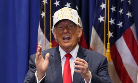 White man wearing navy suit, red tie and white hat holds up his hands.