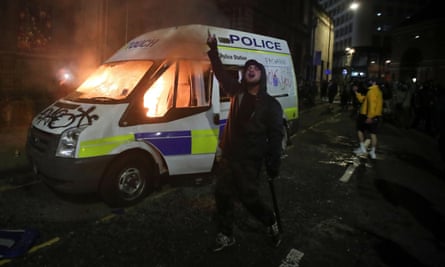A demonstrator gestures in front of a burning police vehicle during the protest.