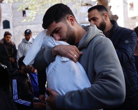 A Palestinian man carries the body of his 5-month-old brother wrapped in a white shroud