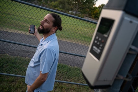 A man stands near a chain-link fence with a device mounted in the foreground.