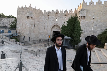 Two Orthodox Jewish men with hats and beards walk up steps in the compound outside the stone mosque building.