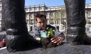 guerrilla gardener plants a flower between the feet of a statue in Parliament Square