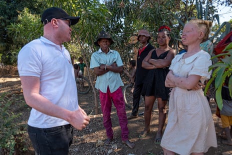 A group of people, two of whom have albinism, talking near some trees