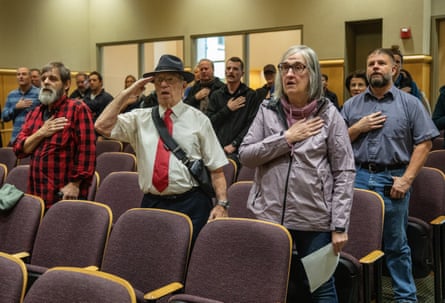 A group of people stand up and place their hands over their hearts
