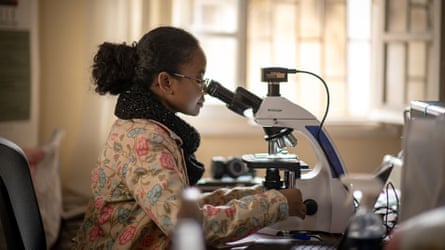 A young African woman sits looking at something through a microscope