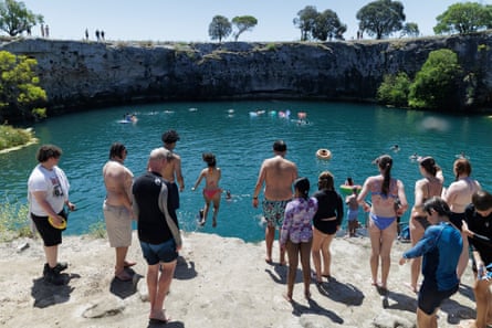 A crowd of swimmers stand on a cliff overlooking blue water