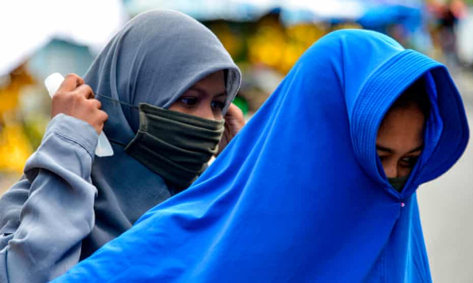 A woman puts on face mask to protect against coronavirus, in Banda Aceh, Indonesia.