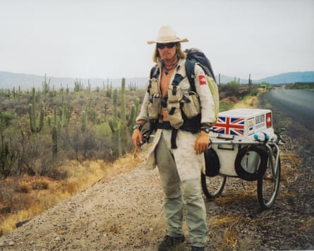 He stands by the side of the road with his baggage trolley, which has a union jack on it